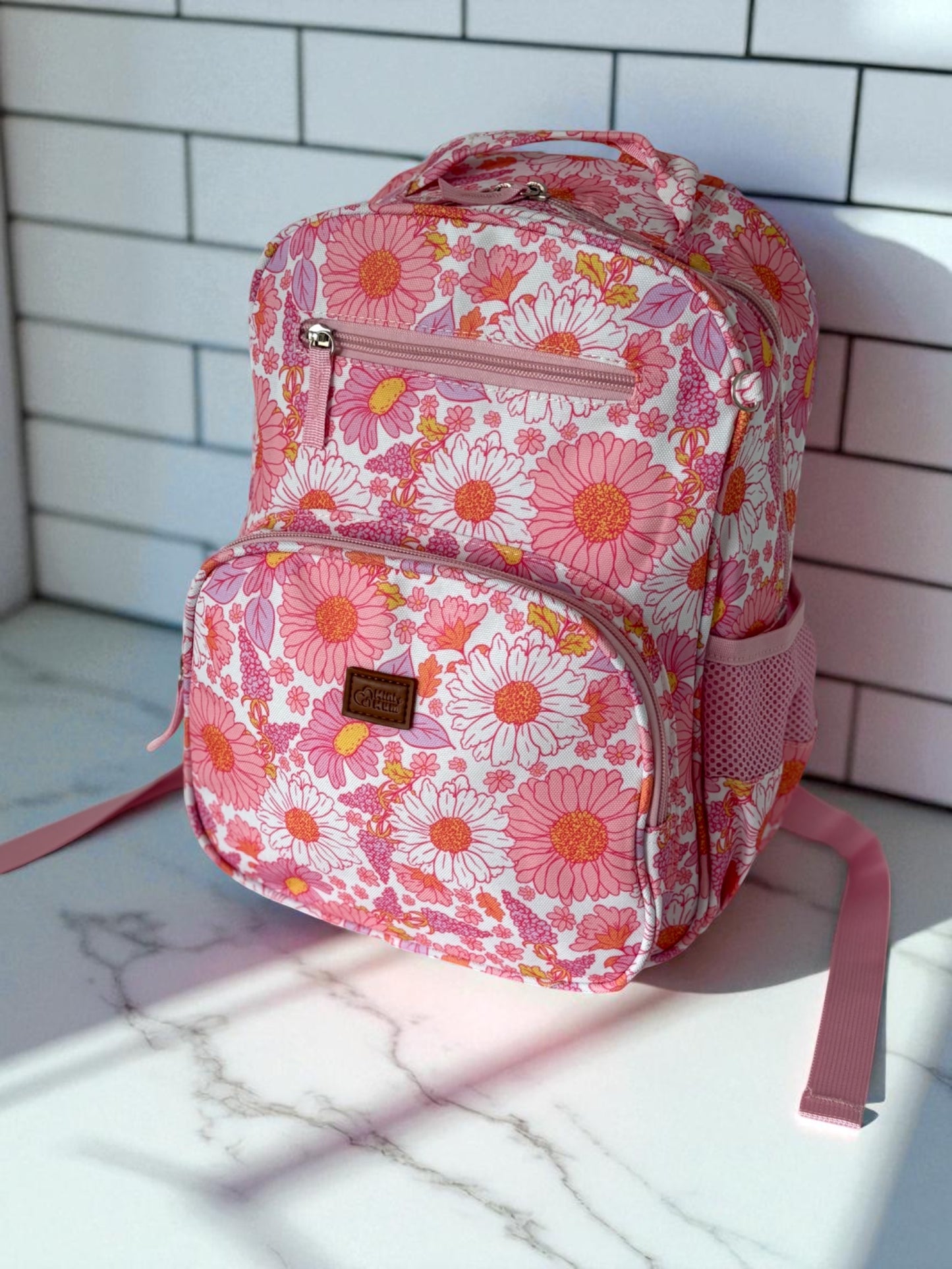 Pink floral backpack on a marble surface with a tiled wall background