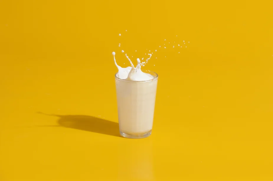 Milk splashing out the top of a glass against a yellow background