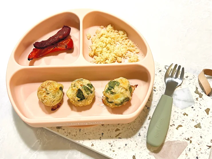Five minute chicken meatballs, cous cous and roasted capsicum in silicone suction plate with baby fork on a terrazzo board - Starting Solids Australia recipe.