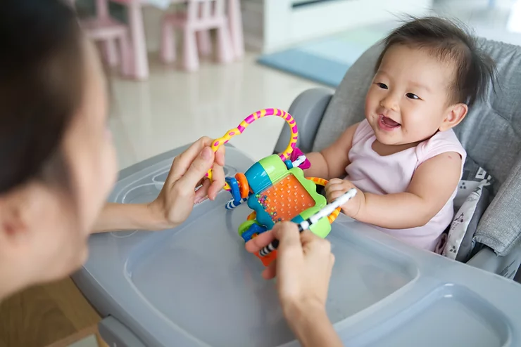 Adult playing with baby in highchair with sensory toy.