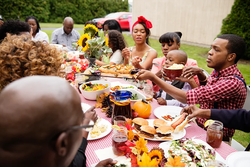African diaspora family mealtime outdoors around a long table.