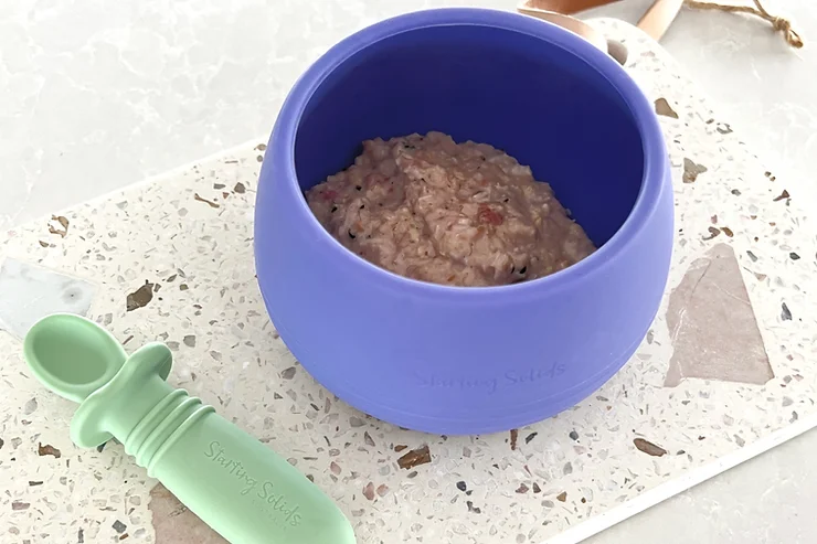 Raspberry Hemp Porridge in purple Suckie Scoop Bowl with green silicone spoon on terrazzo board - Starting Solids Australia recipe.