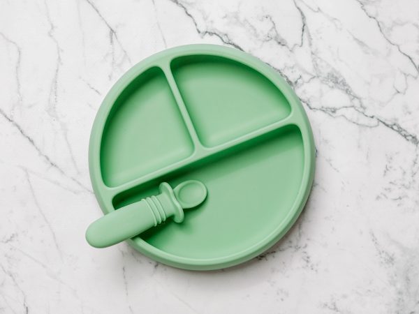 Green Suckie Scoop Divided Plate with Selfie Spoon by Starting Solids Australia, on a marble bench.