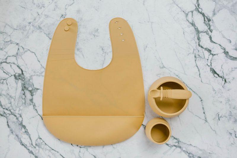 Yellow (Biscoff) silicone bib, cup, bowl and spoon set for babies on a marble bench by Starting Solids Australia