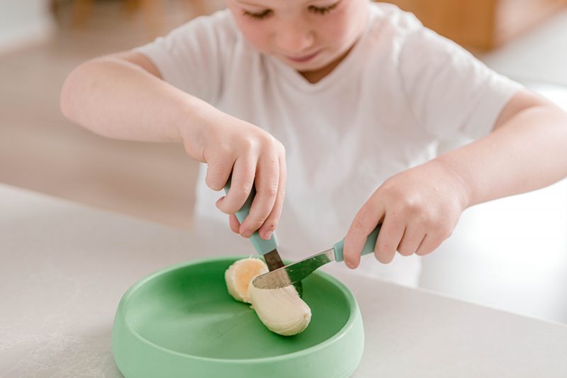 Young Boy chopping banana with Starting Solids Australia's Toddler Silvies on a Suckie Scoop Plate.