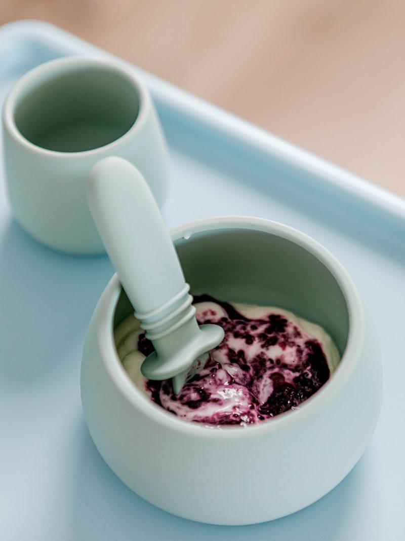 Pastel blue silicone Suckie Scoop Bowl and Selfie Spoon with berries and yoghurt and a Bubbie Cup by Starting Solids Australia on a highchair tray.