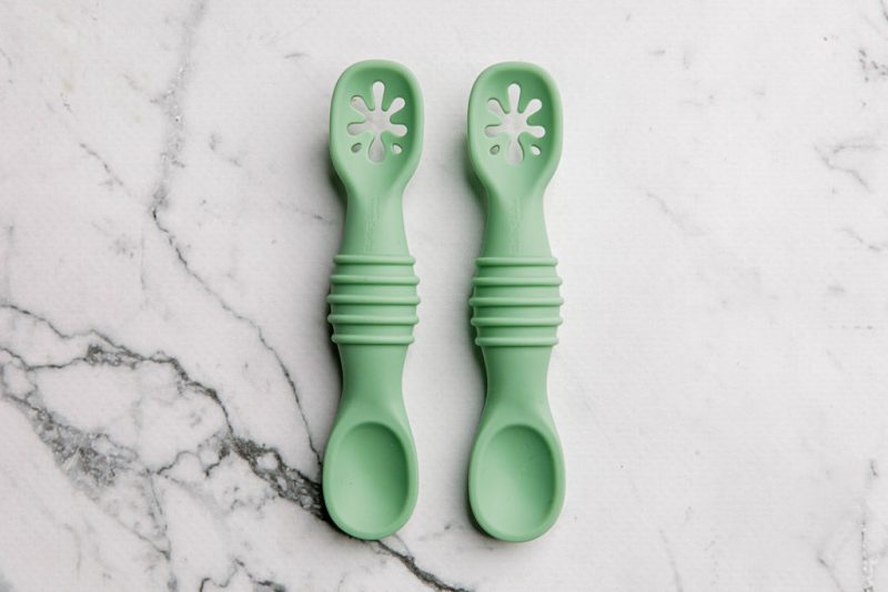 Green silicone sticky spoons for baby on a marble bench by Starting Solids Australia