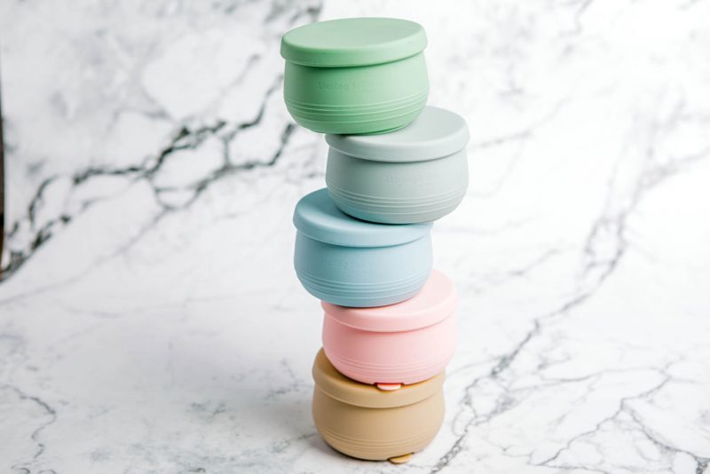 Stack of Suckie Scoop Mini Bowls with lids in assorted colours by Starting Solids Australia on a marble bench.