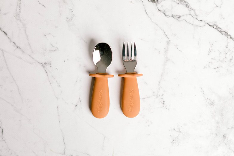 Orange Toddler Silvies (spoon and fork) by Starting Solids Australia on a marble bench.