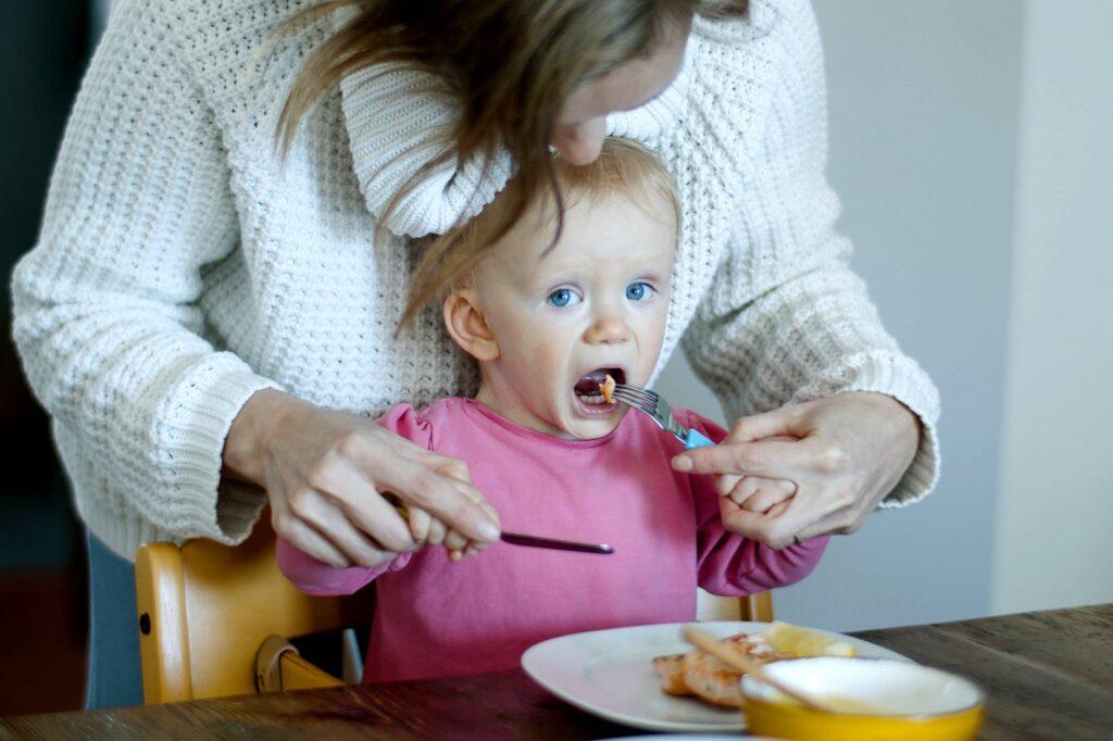 a mother teaching a baby to use cutlery