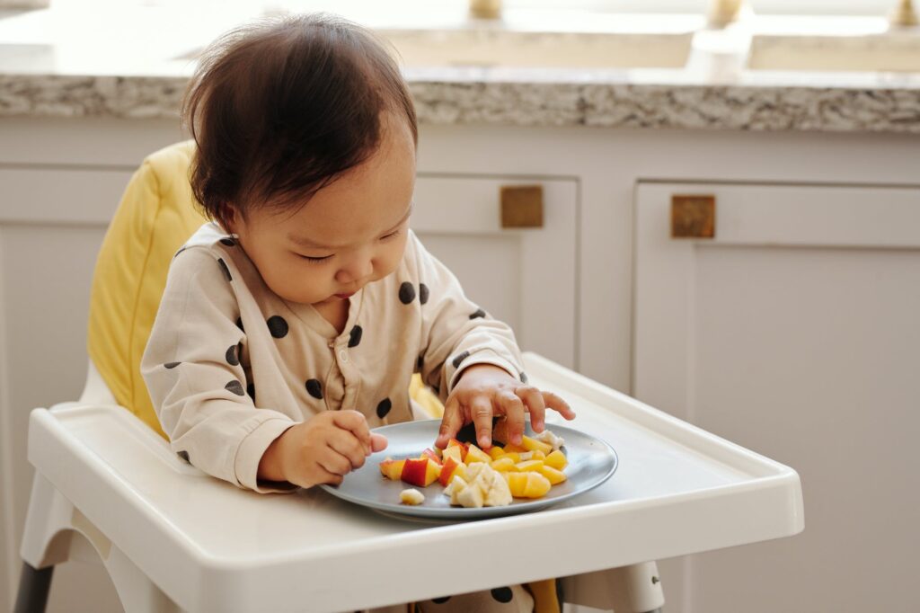 a child sitting on a higher chair eating fruits